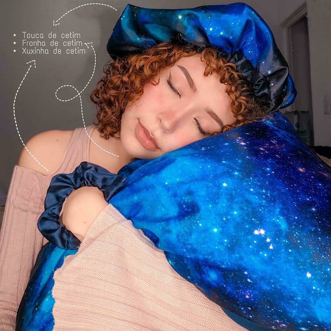 Menina abraçada com travesseiro com fronha de cetim, usando touca de cetim e xuxinha de cetim